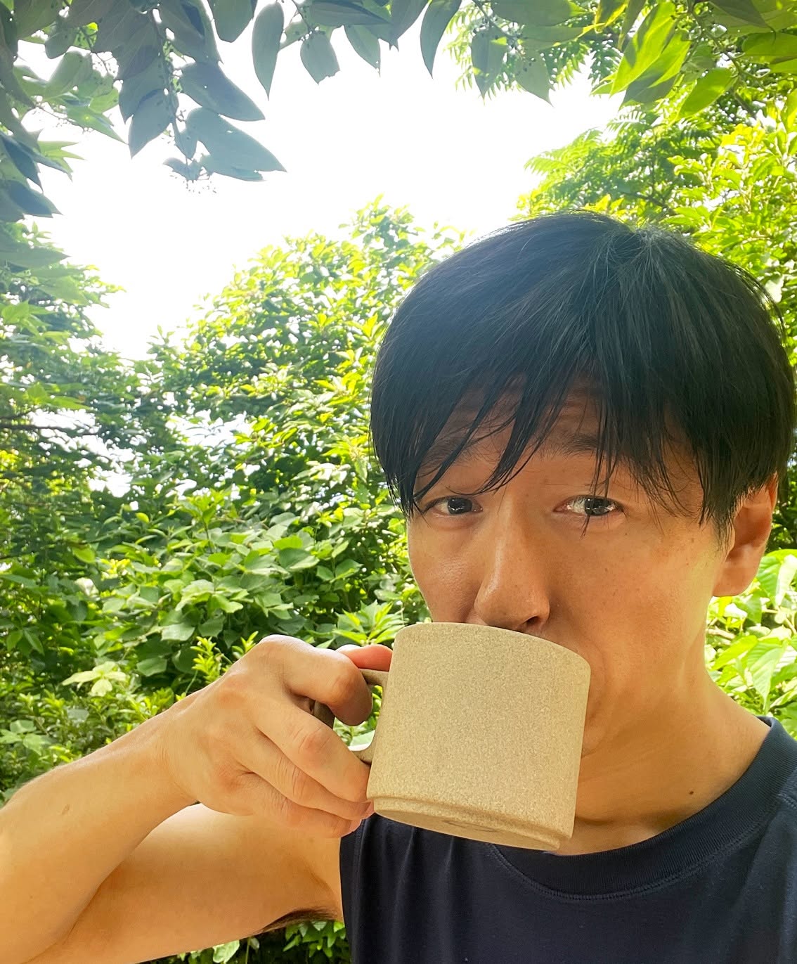 朝の自然光の中でマグカップの飲み物を口にする様子
