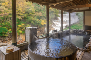 秋の紅葉と渓流を望む露天風呂での疲労回復入浴